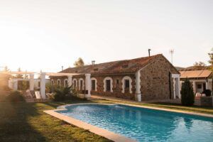La Escapada "Desconecta" ofrece una casa rústica de piedra con techo rojo, piscina y rodeada de árboles, iluminada por el atardecer. Enclavada cerca de Córdoba, este tranquilo refugio promete tranquilidad y relajación. - ForTwo - Planes para parejas