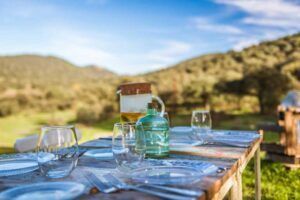 Relájese en la mesa de comedor al aire libre, con elegante cristalería y una jarra, rodeado por las colinas boscosas de Córdoba bajo un cielo azul despejado. Descubra el verdadero bienestar en este remanso de paz con Escapada "Desconecta": Relax y Bienestar en Córdoba. - ForTwo - Planes para parejas