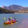 Dos personas disfrutan de la "Excursión Guiada en Kayak en Coll de Nargó: Naturaleza y Aventura en el Pantano", remando en un tranquilo lago rodeado de montañas y bosques, creando una experiencia inolvidable en medio de una serena belleza natural. - ForTwo - Planes para parejas