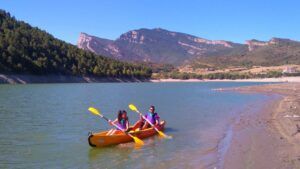 Dos personas disfrutan de la "Excursión Guiada en Kayak en Coll de Nargó: Naturaleza y Aventura en el Pantano", remando en un tranquilo lago rodeado de montañas y bosques, creando una experiencia inolvidable en medio de una serena belleza natural. - ForTwo - Planes para parejas