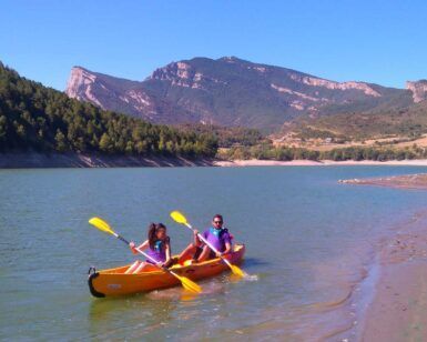 Dos personas disfrutan de la "Excursión Guiada en Kayak en Coll de Nargó: Naturaleza y Aventura en el Pantano", remando en un tranquilo lago rodeado de montañas y bosques, creando una experiencia inolvidable en medio de una serena belleza natural. - ForTwo - Planes para parejas