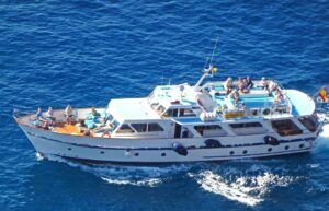 Vista aérea de un yate blanco con gente relajándose en la cubierta, navegando por vibrantes aguas azules cerca de Canarias, disfrutando de una experiencia de Avistamiento de Ballenas en Canarias. - ForTwo - Planes para parejas
