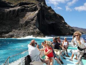 Los turistas en un barco fotografían los espectaculares acantilados de basalto de Canarias bajo un cielo brillante y aguas azules claras, todo mientras esperan un avistamiento de ballenas en Canarias. - ForTwo - Planes para parejas