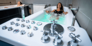 Dos mujeres se entregan a una Experiencia de Relax en Pareja, cada una en su bañera separada llena de agua burbujeante, saboreando la paz de un spa moderno. - ForTwo - Planes para parejas
