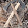 Dos hachas con mangos de madera cruzadas sobre una pila de troncos muestran el arte de "Forja Tu Propia Hacha: Una Experiencia Única". - ForTwo - Planes para parejas