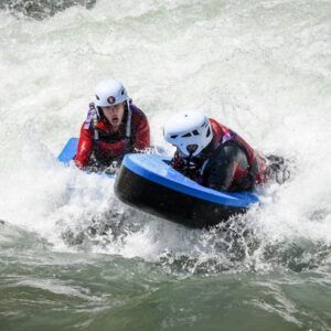 En medio de la aventura del río, dos buscadores de emociones con cascos navegan expertamente por los rápidos de Huesca, mostrando emoción y concentración en su emocionante experiencia "Hidrospeed en Huesca: Descenso de aventura en el río para amantes de la adrenalina". - ForTwo - Planes para parejas