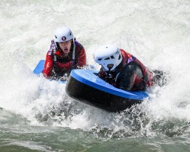 En medio de la aventura del río, dos buscadores de emociones con cascos navegan expertamente por los rápidos de Huesca, mostrando emoción y concentración en su emocionante experiencia "Hidrospeed en Huesca: Descenso de aventura en el río para amantes de la adrenalina". - ForTwo - Planes para parejas