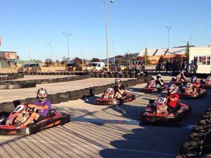 Los corredores en karts individuales recorren una pista al aire libre rodeada de barreras de neumáticos bajo un cielo despejado, encarnando la emoción del karting con "Karting en Jaca: Karts Individuales, Biplaza y Junior para Toda la Familia. - ForTwo - Planes para parejas