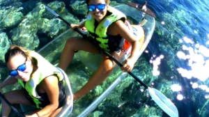 Dos personas navegan en un Kayak Transparente en Radazul: Explora el fondo marino de Tenerife sobre aguas turquesas, con chalecos salvavidas y gafas de sol, sonriendo a la cámara con el impresionante fondo marino brillando debajo de ellos. - ForTwo - Planes para parejas