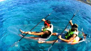 Dos personas con chalecos salvavidas realizan la excursión "Kayak Transparente en Radazul: Explora el fondo marino de Tenerife", deslizándose sobre vibrantes aguas azules sobre un impresionante paisaje submarino bajo un cielo soleado. - ForTwo - Planes para parejas