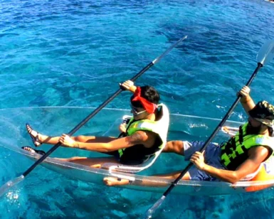 Dos personas con chalecos salvavidas realizan la excursión "Kayak Transparente en Radazul: Explora el fondo marino de Tenerife", deslizándose sobre vibrantes aguas azules sobre un impresionante paisaje submarino bajo un cielo soleado. - ForTwo - Planes para parejas