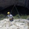 Con un casco y asegurado con cuerdas, alguien se sienta en el borde del acantilado con vistas a la entrada de la cueva del Barranco de la Luna, preparado para vivir una experiencia emocionante con Multiaventura en el Barranco de la Luna. - ForTwo - Planes para parejas