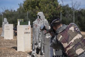 En un entorno forestal cerca de Mallorca, una persona camuflada disfruta del paintball entre barreras de lápidas, capturando la esencia de "Paintball a 10 minutos de Mallorca: Aventura y Diversión. - ForTwo - Planes para parejas