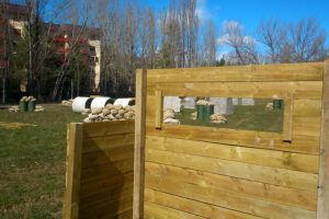 Barricadas de paintball de madera se encuentran sobre un campo de césped en Paintball en Jaca: Diversión y Estrategia en Escenarios de Alto Nivel, con sacos de arena y árboles que mejoran la diversión estratégica para todos los participantes. - ForTwo - Planes para parejas