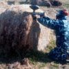 En Jaca, un jugador con traje de camuflaje se arrodilla junto a un fardo de heno y apunta con precisión su pistola de paintball. "Paintball en Jaca: Diversión y Estrategia en Escenarios de Alto Nivel" transforma el campo en un emocionante campo de batalla. - ForTwo - Planes para parejas