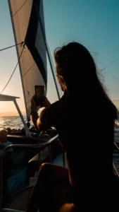 Una mujer silueta captura una impresionante puesta de sol en un velero durante el tranquilo "Paseo en Barco al Atardecer en Mallorca: Sunset Tour", con el sereno océano y el cielo de fondo, evocando la encantadora belleza de Mallorca. - ForTwo - Planes para parejas