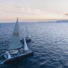 Durante un Paseo en Barco al Atardecer en Mallorca: Sunset Tour, dos veleros con velas blancas se deslizan sobre el mar en calma con las serenas montañas de Mallorca en el horizonte. - ForTwo - Planes para parejas
