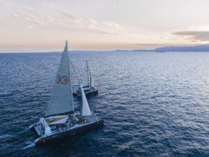 Durante un Paseo en Barco al Atardecer en Mallorca: Sunset Tour, dos veleros con velas blancas se deslizan sobre el mar en calma con las serenas montañas de Mallorca en el horizonte. - ForTwo - Planes para parejas