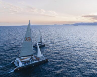 Durante un Paseo en Barco al Atardecer en Mallorca: Sunset Tour, dos veleros con velas blancas se deslizan sobre el mar en calma con las serenas montañas de Mallorca en el horizonte. - ForTwo - Planes para parejas