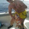Un hombre con pantalones cortos amarillos, mostrando su amor por la pesca, sostiene con orgullo una caña y un pez grande mientras está a bordo de su barco frente a la costa de Tenerife durante Pesca Deportiva en Tenerife con SEA PASSION. - ForTwo - Planes para parejas
