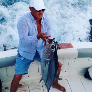 Un hombre vestido de manera informal sostiene con orgullo un gran pez a bordo de su barco SEA PASSION, navegando por las aguas de Tenerife entre salpicaduras, resaltando la emoción de Pesca Deportiva en Tenerife con SEA PASSION. - ForTwo - Planes para parejas