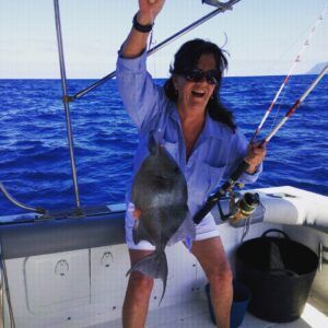 Bajo el cielo soleado de Tenerife, una mujer sostiene con alegría un gran pez capturado durante su aventura de Pesca Deportiva en Tenerife con SEA PASSION. El océano se extiende tras ella mientras luce unas elegantes gafas de sol, disfrutando plenamente de la experiencia. - ForTwo - Planes para parejas