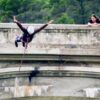 Alguien disfruta de "Puenting en Huesca: Vive la Caída Libre en Murillo de Gállego" desde un puente, mientras otra persona observa asombrada desde un costado. - ForTwo - Planes para parejas