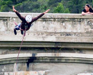 Alguien disfruta de "Puenting en Huesca: Vive la Caída Libre en Murillo de Gállego" desde un puente, mientras otra persona observa asombrada desde un costado. - ForTwo - Planes para parejas