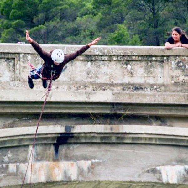 Alguien disfruta de "Puenting en Huesca: Vive la Caída Libre en Murillo de Gállego" desde un puente, mientras otra persona observa asombrada desde un costado. - ForTwo - Planes para parejas