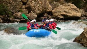 Los aventureros se enfrentan a emocionantes corrientes fluviales en balsas de un azul brillante con Sarratillo, mientras su risa resuena en el impresionante paisaje de Huesca en el Pirineo Aragonés durante "Rafting en Huesca: Aventura y Diversión. - ForTwo - Planes para parejas