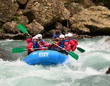 Los aventureros se enfrentan a emocionantes corrientes fluviales en balsas de un azul brillante con Sarratillo, mientras su risa resuena en el impresionante paisaje de Huesca en el Pirineo Aragonés durante "Rafting en Huesca: Aventura y Diversión. - ForTwo - Planes para parejas
