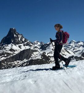 Utilizando "Raquetas de Nieve en Huesca para Principiantes: Ruta Circular en Somport", una persona explora un impresionante paisaje nevado cerca del paso de Somport con majestuosos picos y un cielo azul claro al fondo. - ForTwo - Planes para parejas