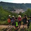 Los excursionistas con mochilas admiran un pueblo pintoresco y las exuberantes colinas verdes que aparecen en "Rutas de senderismo en Valencia: Naturaleza a tu ritmo". - ForTwo - Planes para parejas