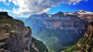 Explora las impresionantes "Rutas en 4x4 y Senderismo por el Parque Nacional de Ordesa", con espectaculares paisajes montañosos con acantilados, valles verdes y picos nevados bajo un cielo parcialmente nublado. - ForTwo - Planes para parejas