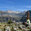 Dos personas admiran un vasto paisaje montañoso sobre un terreno rocoso bajo un cielo azul claro, perfecto para practicar senderismo con las "Rutas en 4x4 y Senderismo por el Parque Nacional de Ordesa. - ForTwo - Planes para parejas