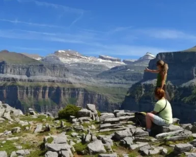Dos personas admiran un vasto paisaje montañoso sobre un terreno rocoso bajo un cielo azul claro, perfecto para practicar senderismo con las "Rutas en 4x4 y Senderismo por el Parque Nacional de Ordesa. - ForTwo - Planes para parejas