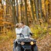 Una pareja explora las pintorescas Rutas en Quad por la Alta Montaña de Huesca en un vehículo todo terreno, rodeados de un vibrante follaje naranja y hojas caídas en un bosque otoñal. - ForTwo - Planes para parejas