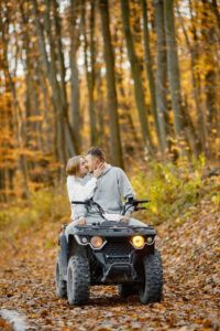 Una pareja explora las pintorescas Rutas en Quad por la Alta Montaña de Huesca en un vehículo todo terreno, rodeados de un vibrante follaje naranja y hojas caídas en un bosque otoñal. - ForTwo - Planes para parejas
