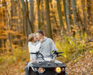 Una pareja explora las pintorescas Rutas en Quad por la Alta Montaña de Huesca en un vehículo todo terreno, rodeados de un vibrante follaje naranja y hojas caídas en un bosque otoñal. - ForTwo - Planes para parejas