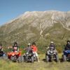 Los pilotos de cuatriciclos encarnan el espíritu aventurero de Rutas en Quad por la Alta Montaña de Huesca, posando ante una majestuosa Alta Montaña bajo un cielo azul despejado. - ForTwo - Planes para parejas
