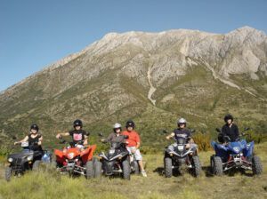 Los pilotos de cuatriciclos encarnan el espíritu aventurero de Rutas en Quad por la Alta Montaña de Huesca, posando ante una majestuosa Alta Montaña bajo un cielo azul despejado. - ForTwo - Planes para parejas