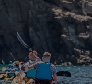 Los kayakistas con chalecos azules disfrutan de una soleada aventura de safari, remando cerca de acantilados rocosos en el "Safari en Kayak y Snorkel en Tenerife". - ForTwo - Planes para parejas