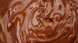 Un primer plano del chocolate gourmet derretido y suave revela su textura brillante y cremosa: un verdadero deleite para cualquiera que asista al Taller de Cata y Elaboración de Chocolates Gourmet en Barcelona. - ForTwo - Planes para parejas