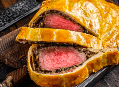 El Taller de Cocina para Sorprender a Tus Invitados ofrece una experiencia elegante y gourmet con filetes Wellington en rodajas sobre una tabla de madera, mostrando carne a medio cocinar envuelta en masa con una sabrosa capa de champiñones. - ForTwo - Planes para parejas