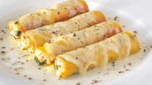 Cuatro canelones con salsa cremosa y hierbas sobre un plato blanco, perfectos para mostrar tus habilidades culinarias con "Taller de Cocina para Sorprender a Tus Invitados". - ForTwo - Planes para parejas