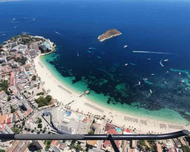El "Tour en Helicóptero por Mallorca" ofrece una impresionante vista aérea de playas de arena, aguas turquesas con barcos que se mecen suavemente y una pequeña isla distante: una vista verdaderamente inolvidable. - ForTwo - Planes para parejas