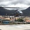 Un helicóptero aterriza cerca de un pintoresco pueblo mientras los majestuosos Acantilados de Los Gigantes se elevan bajo un cielo nublado durante el Tour en Helicóptero sobre los Acantilados de Los Gigantes y el Teide. - ForTwo - Planes para parejas