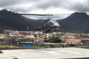 Un helicóptero aterriza cerca de un pintoresco pueblo mientras los majestuosos Acantilados de Los Gigantes se elevan bajo un cielo nublado durante el Tour en Helicóptero sobre los Acantilados de Los Gigantes y el Teide. - ForTwo - Planes para parejas