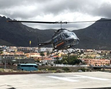 Un helicóptero aterriza cerca de un pintoresco pueblo mientras los majestuosos Acantilados de Los Gigantes se elevan bajo un cielo nublado durante el Tour en Helicóptero sobre los Acantilados de Los Gigantes y el Teide. - ForTwo - Planes para parejas