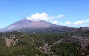 Experimente un impresionante recorrido en helicóptero sobre el majestuoso volcán Teide, mientras se eleva sobre colinas boscosas bajo un cielo azul claro. - ForTwo - Planes para parejas